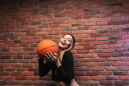 Portrait of lovely girl 20s standing against brick wall and holding basketballの写真素材
