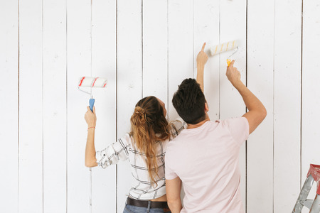 Photo of young couple man and woman painting white wall and making renovation using paint rollersの写真素材