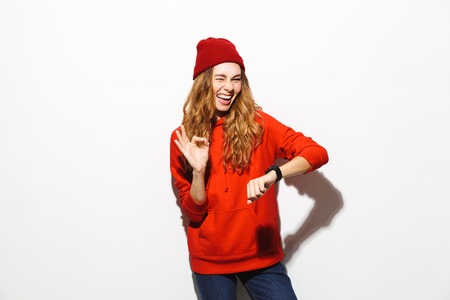 Portrait of an excited girl wearing hoodie isolated over white background, showing wrist watch