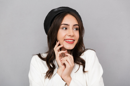 Portrait of a delighted young woman wearing beret standing isolated over gray background, looking awayの写真素材