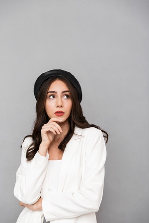 Portrait of a pensive young woman wearing beret standing isolated over gray background, looking away at copy spaceの写真素材