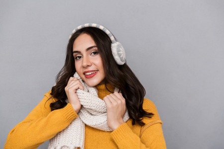 Portrait of a lovely young woman wearing sweater and scarf isolated over gray backgroundの写真素材