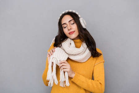 Portrait of a lovely young woman wearing sweater and scarf isolated over gray backgroundの写真素材