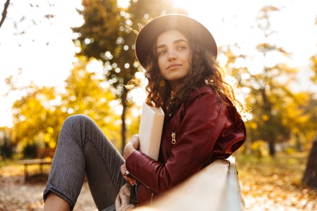 Image of an amazing beautiful woman sitting on a bench in park reading book.の写真素材