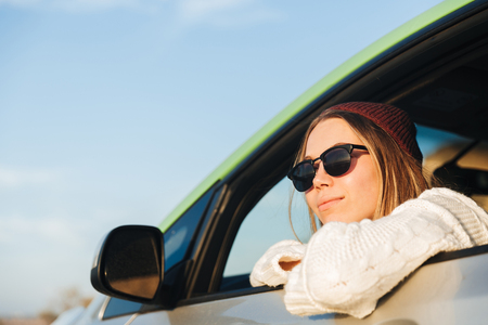 Smiling young girl driving a car during sunset, looking at the windowの写真素材
