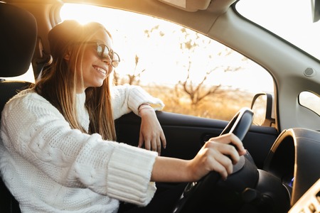 Smiling young girl driving a car during sunsetの写真素材