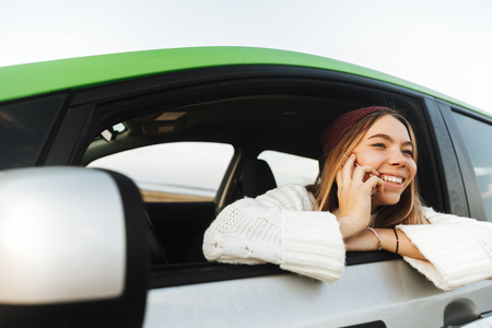 Beautiful young woman talking on mobile phone while sitting in a carの写真素材