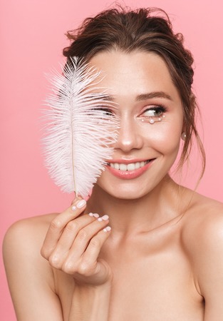 Photo of a beautiful happy cheerful young woman posing isolated over pink wall background holding feather leaf.の写真素材