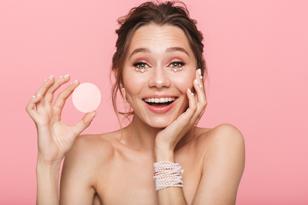 Photo of a beautiful shocked happy young woman posing isolated over pink wall background holding cotton disk.の写真素材