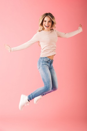 Full length portrait of a happy young woman wearing sweater jump isolated over pink background