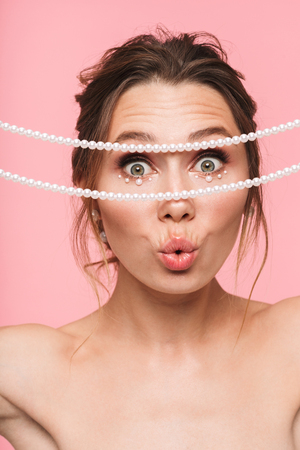 Beauty portrait of an attractive young topless woman posing isolated over pink background, wearing white pearlsの写真素材