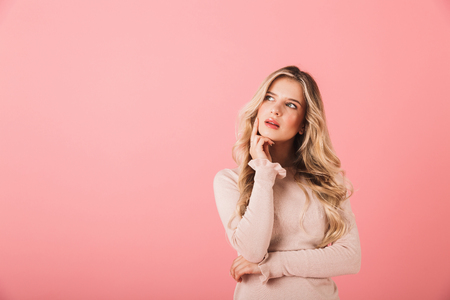 Portrait of a cheerful young woman wearing sweater standing isolated over pink background, looking away at copy spaceの写真素材