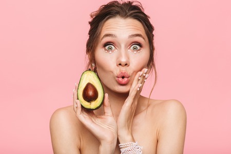 Beauty portrait of an attractive healthy young topless woman posing with an avocado isolated over...