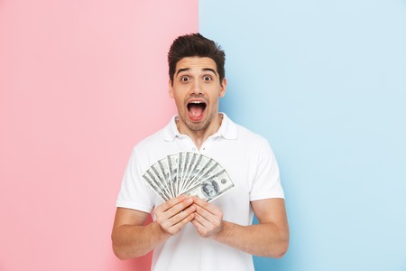 Smiling young man standing isolated over two colored background, showing money banknotesの写真素材