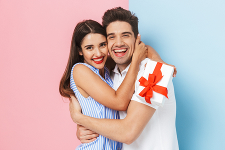 Happy young couple standing isolated over two colored background, celebrating, holding gift box, huggingの写真素材