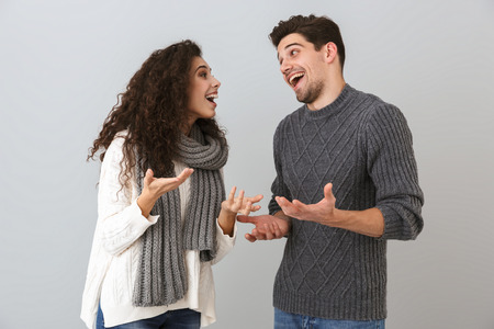 Portrait of cheerful couple man and woman smiling and talking to each other isolated over gray...