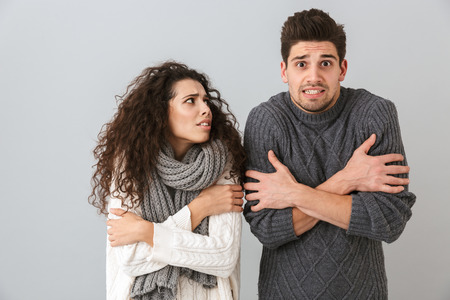Photo of frozen couple man and woman wearing scarfs trembling and hugging themselves isolated over...