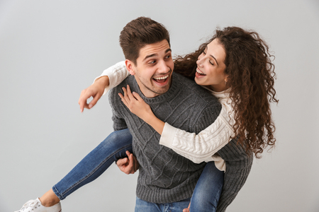Image of joyful couple having fun and while man piggybacking attractive woman isolated over gray backgroundの写真素材