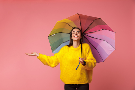 Cheerful young woman wearing sweater holding an umbrella isolated over pink backgroundの写真素材