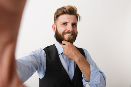 Image of a young bearded man standing isolated over white wall background make selfie by camera.の写真素材