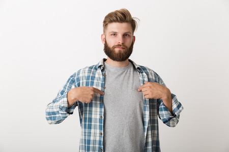 Worried bearded man dressed in plaid shirt standing isolated over white background, pointing fingers...