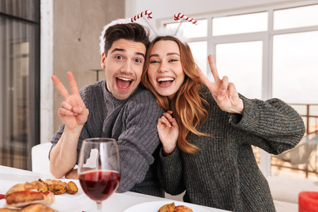 Beautiful european couple celebrating New Year at home and drinking wine while sitting at tableの写真素材