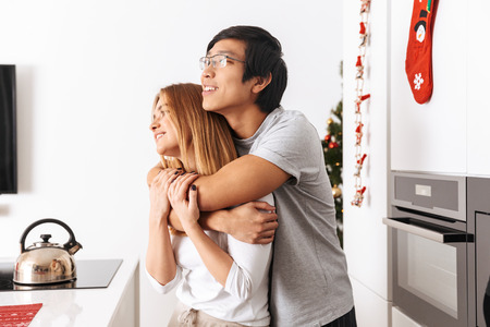 Image of beautiful couple man and woman standing in bright kitchen and hugging togetherの写真素材