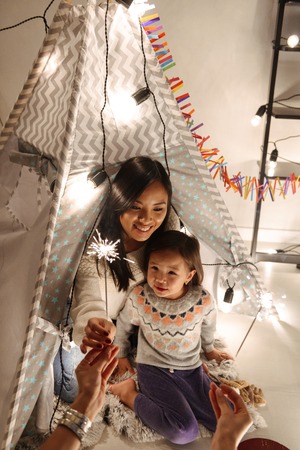 Happy young asian woman with her little daughter girl sitting on floor holding bengal lights....