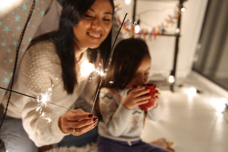 Photo of a happy young asian woman with her little daughter girl sitting on floor holding bengal lights. Christmas concept.の写真素材
