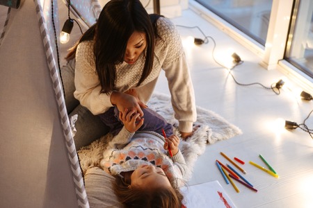 Photo of a happy young asian woman with her little daughter having fun on floor. Christmas concept.の写真素材