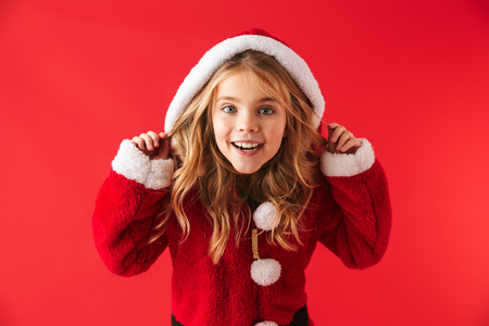 Cute cheerful little girl wearing Christmas costume isolated over red backgroundの写真素材