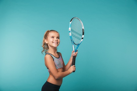 Cheerful young sports girl playing tennis isolated over blue backgroundの写真素材