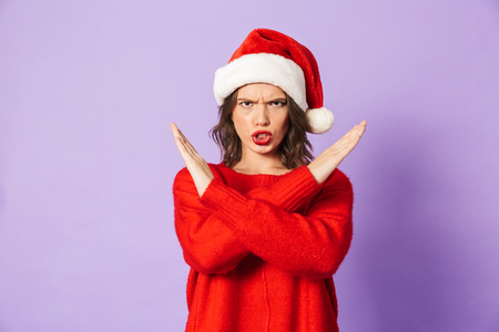 Portrait of a displeased young woman wearing christmas hat isolated over purple background showing stop gesture.の写真素材