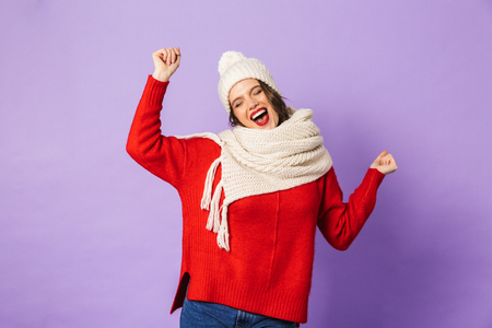 Portrait of an excited happy young woman wearing winter hat isolated over purple background.の写真素材