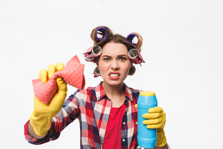 Angry housewife with curlers in hair standing isolated over white background, holding detergentsの写真素材