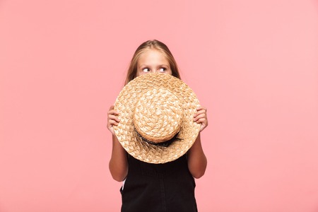 Portrait of a cheerful little girl wearing summer hat isolated over pink background, looking awayの写真素材