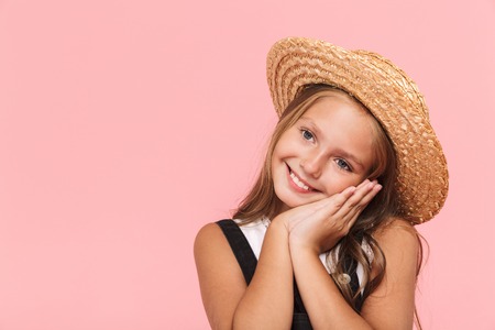 Portrait of a cheerful little girl wearing summer hat isolated over pink backgroundの写真素材