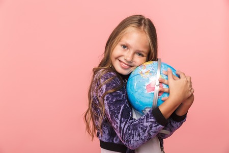Smiling little girl standing isolated over pink background, holding earth globeの写真素材