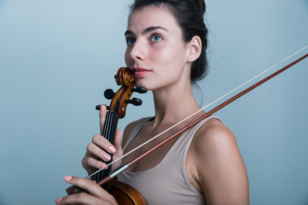 Close up portrait of a beautiful young woman posing with a violin isolated over blue backgroundの写真素材