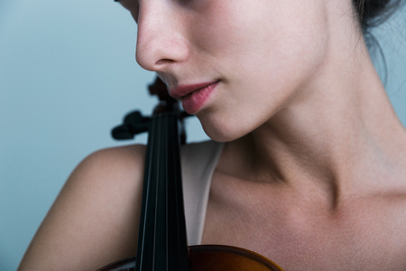 Cropped image of a beautiful young woman posing with a violin isolated over blue backgroundの写真素材
