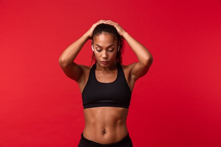 Image of a beautiful young african sports fitness woman posing isolated over red wall background listening music with earphones.の写真素材