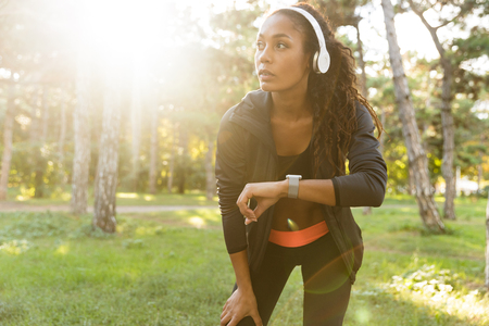 Image of skinny woman 20s wearing black tracksuit and headphones walking through green parkの写真素材