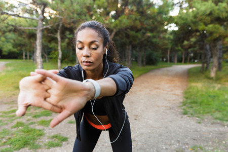 Portrait of energetic sportswoman 20s wearing black tracksuit doing exercises and stretching her...