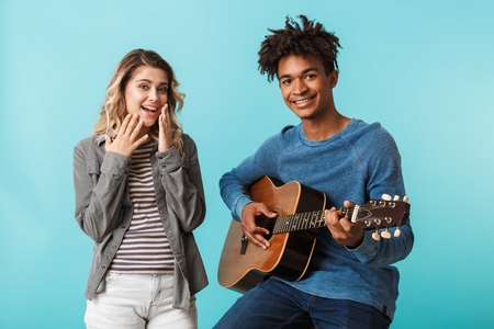 Happy young multiethninc couple together, playing a guitar isolated over blue backgroundの写真素材