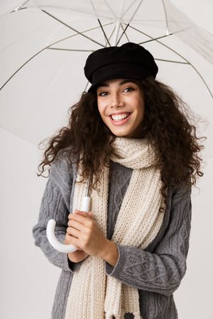 Excited young woman wearing autumn clothes standing isolated over white background, holding an open umbrellaの写真素材