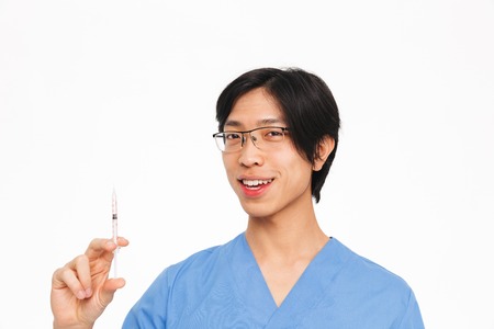 Smiling asian man doctor wearing uniform standing isolated over white background, showing a syringeの写真素材