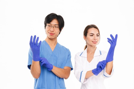 Smiling doctors couple wearing uniform and rubber gloves standing isolated over white backgroundの写真素材