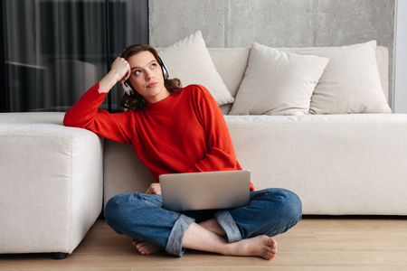 Tired young casually dressed woman sitting on a floor at home, studying with laptop computerの写真素材