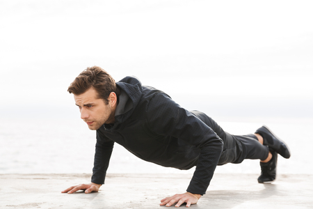 Handsome confident young sportsman working out at the beach, doing push-ups