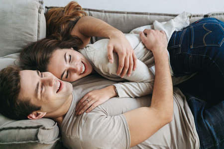 Happy young couple relaxing on a couch at home, embracingの写真素材
